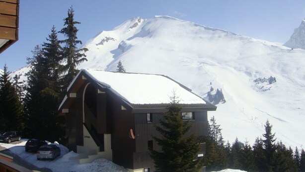 A wooden cabin with a snow-covered roof, surrounded by evergreen trees, set against a backdrop of a snow-covered mountain. - APARTMENT MANIGOD - The ÉTALE (La Clusaz) to SKI FOOT (MANIGOD)