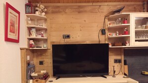 A wooden-paneled room with a flat-screen TV mounted on a cabinet, surrounded by shelves with various items. - APARTMENT MANIGOD - The ÉTALE (La Clusaz) to SKI FOOT (MANIGOD)