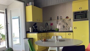 Een moderne keuken met gele kastjes, een inbouwoven en een eethoek met een ronde tafel en kleurrijke stoelen.