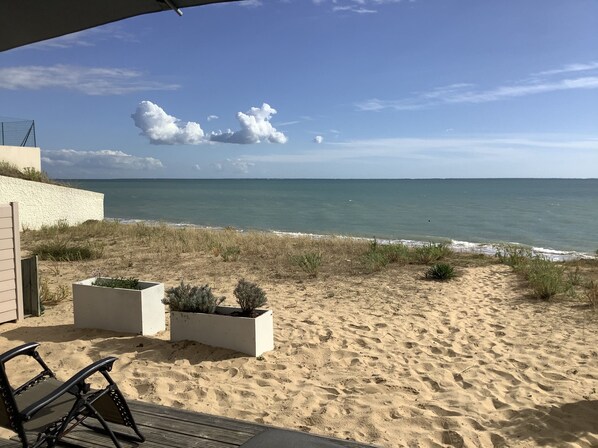 Blick auf einen Strand mit einer Terrassenfläche, inklusive einer Bank und Pflanzgefäßen.