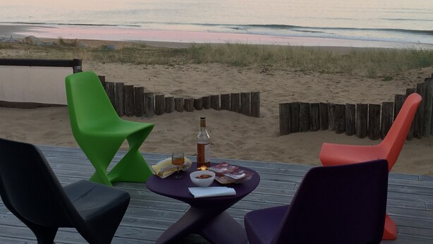 Een zitzone aan het strand met een tafel, stoelen en een fles drank.