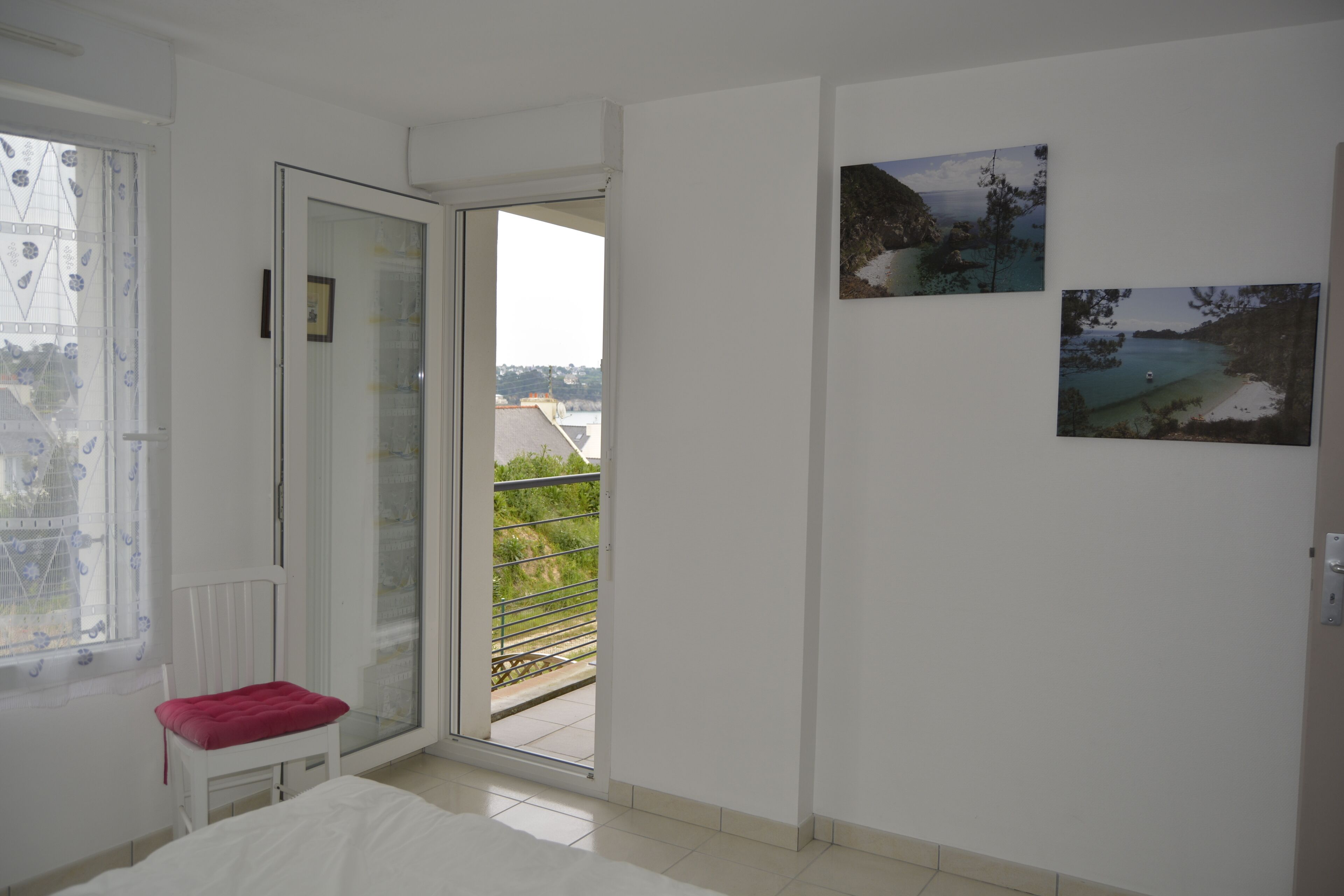 Une chambre avec une porte-fenêtre coulissante donnant sur un balcon. Deux tableaux encadrés sont accrochés au mur.