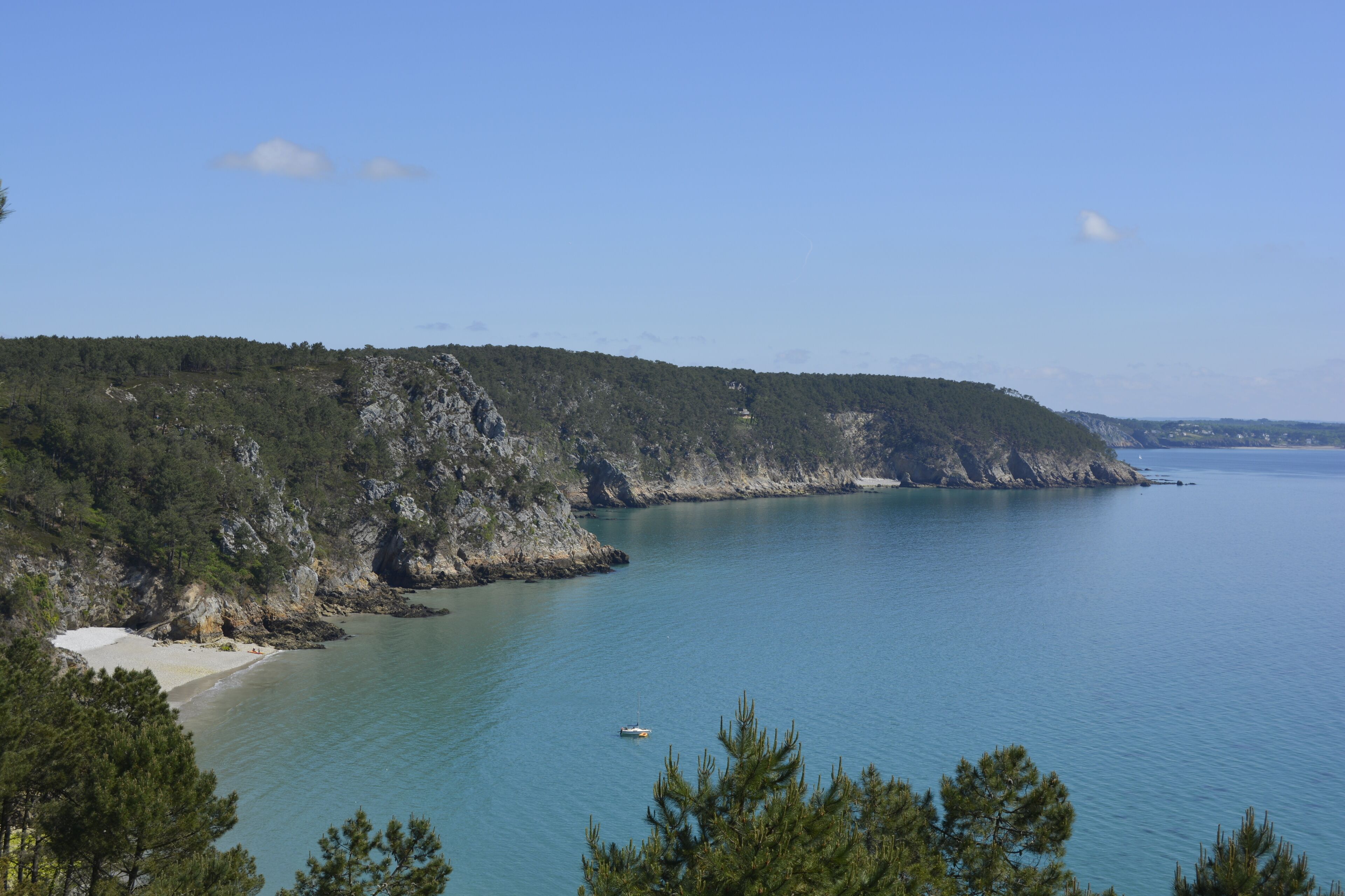 A coastal landscape with a beach, rocky cliffs, and a clear sky.