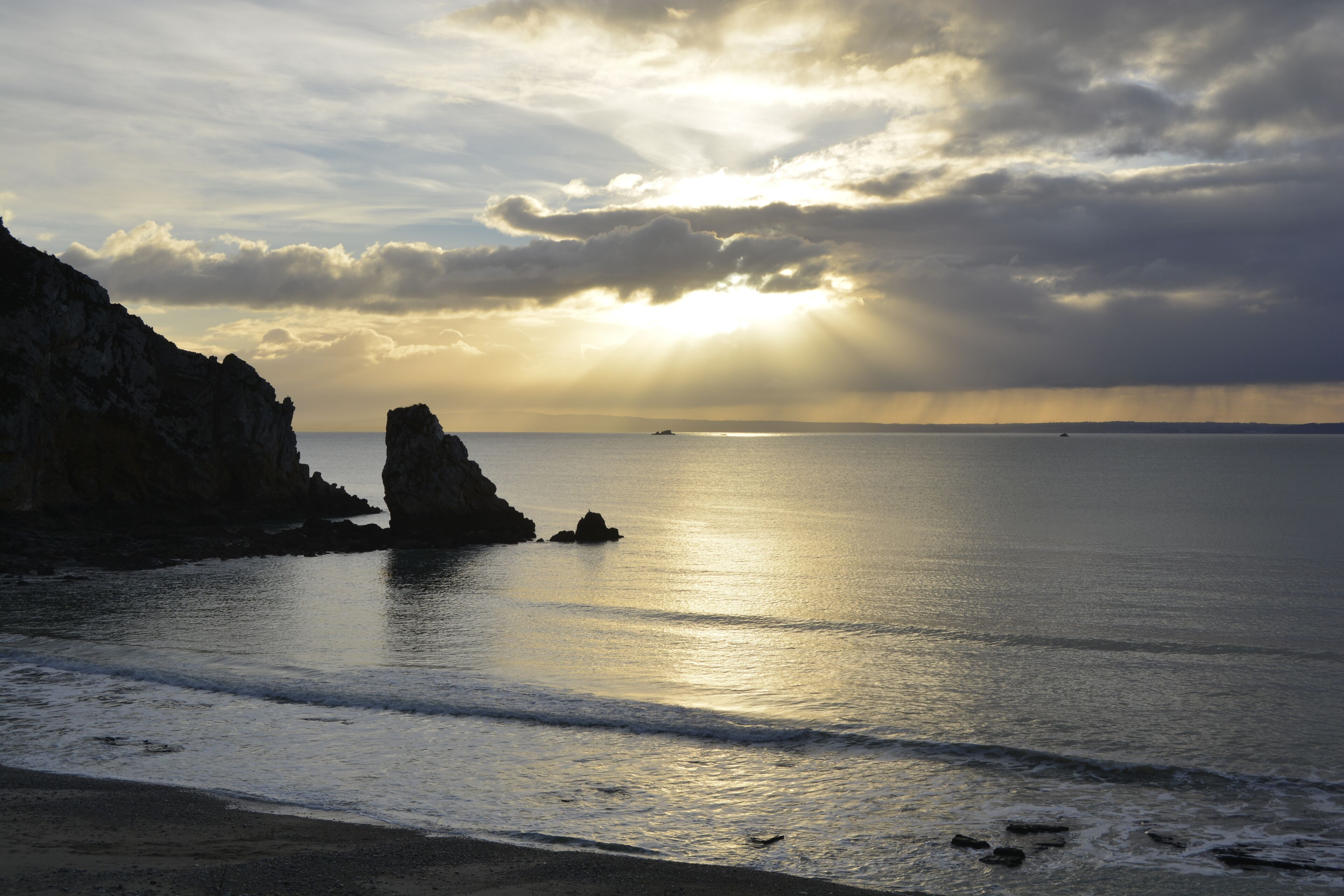 A coastal landscape with cliffs, calm sea, and a sunset.