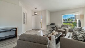 A modern living room with a sofa, armchairs, a coffee table, a TV, and a keyboard on a stand.