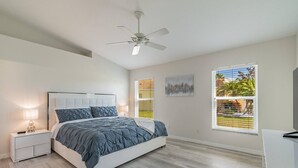 A bedroom with a bed, nightstand, ceiling fan, and two windows with blinds.