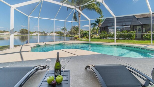 A pool area with a covered section, two lounge chairs, a bottle of wine, and two apples on a table.