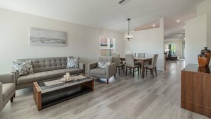 A modern living room with a grey sofa, a coffee table, and a dining area with a wooden table and chairs.