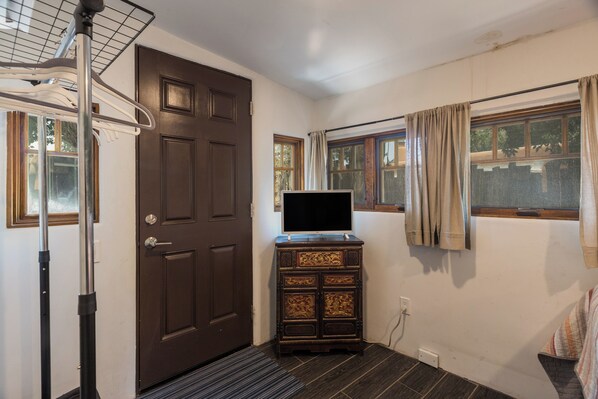 A room with a wooden door, a television on a cabinet, and a window with curtains. - Whyte Casita off the Plaza (Santa Fe)