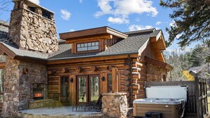 Une cabane en rondins avec une cheminée en pierre, un jacuzzi et un espace patio.