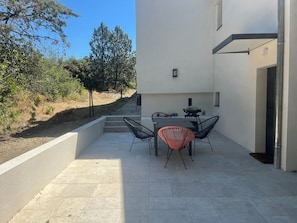 An outdoor patio with a table and chairs, a barbecue grill, and a view of the surrounding landscape.