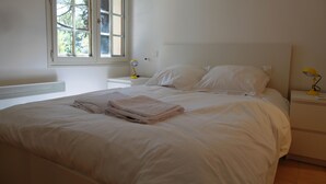 A bedroom with a large bed, white bedding, a bedside table with a lamp, and a window with a view of trees. - Family home, large pool – 15 min to Avignon (Villeneuve-Lès-Avignon)