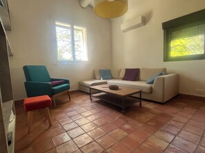 Ein Wohnzimmer mit einer Couch, einem Sessel, einem Couchtisch und einem Fenster mit Jalousien.