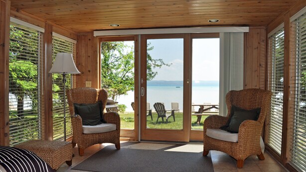 Una habitación con vista a un lago, sillas de mimbre, una lámpara y una cama.