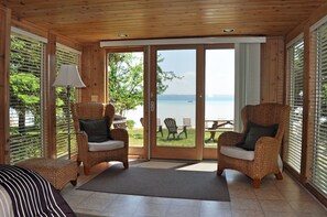 A room with a view of a lake, wicker chairs, a lamp, and a bed.