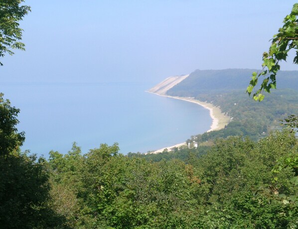 A coastal landscape with a beach, dense greenery, and a clear sky.