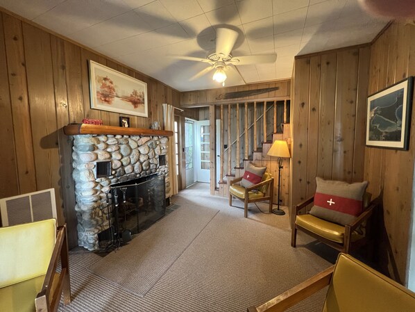 A cozy room with a stone fireplace, wooden walls, a ceiling fan, and a framed picture on the wall.