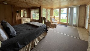 Un dormitorio de cabaña de madera con cama, cómoda, silla y vistas al exterior.