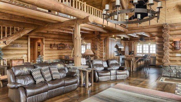 A log cabin interior with a leather sofa, wooden staircase, and a dining area. - Stone Lodge-Panoramic Views, Lots of Space! (Lead)