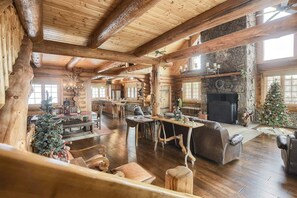 A log cabin interior with a fireplace, wooden furniture, and a Christmas tree.