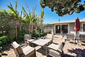 Relax and socialize in this serene outdoor space with wicker chairs, a table, and lush greenery.
