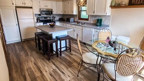 A spacious kitchen with white cabinets, a wooden floor, a dining area with wicker chairs, and a ceiling fan. - ALL OCCASION Central WI Home (Rothschild)