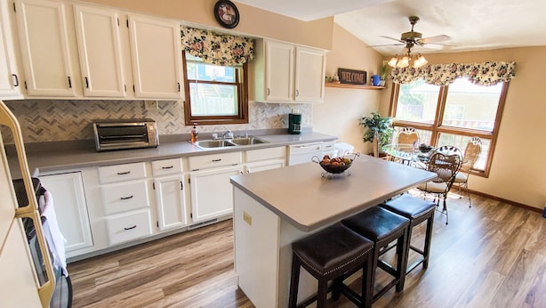 A kitchen with white cabinets, a central island with stools, a coffee maker, and a clock on the wall. - ALL OCCASION Central WI Home (Rothschild)