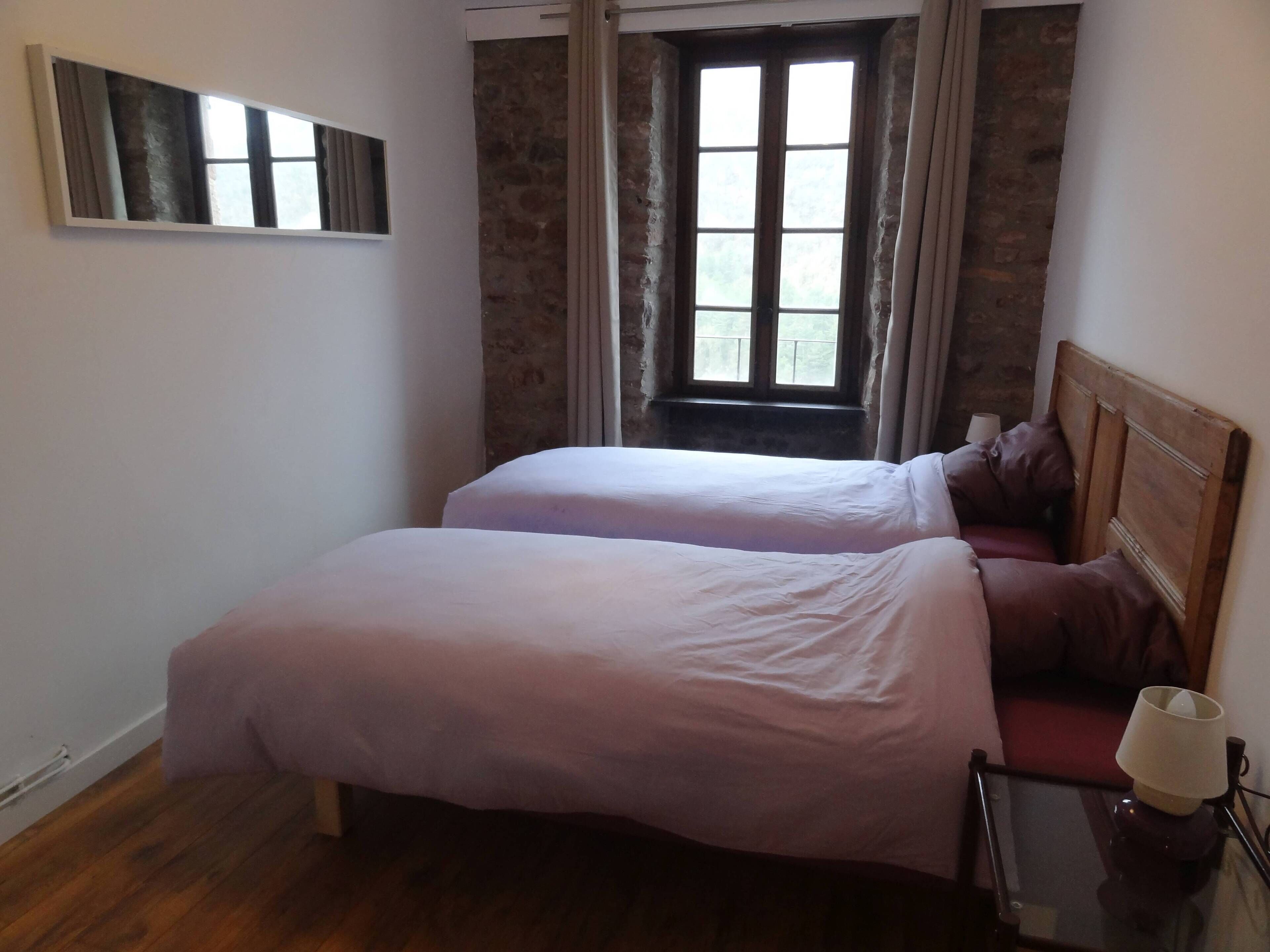 Un dormitorio con dos camas, una ventana con cortinas, un cabecero de madera y una mesita de noche con una lámpara.
