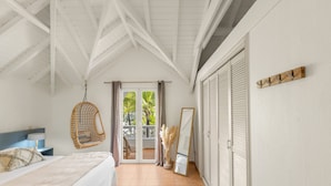 Un dormitorio con cama, sillón colgante, espejo y puertas correderas que dan a un balcón.