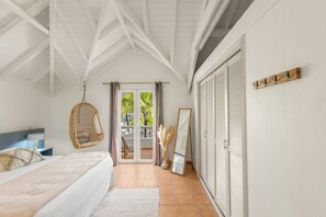 Une chambre à coucher comprenant un lit, un fauteuil suspendu, un miroir et des portes coulissantes donnant sur un balcon.