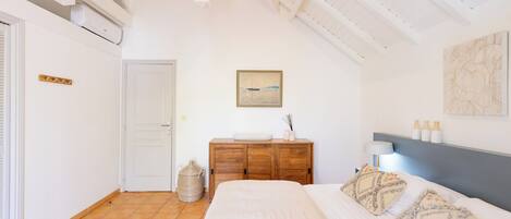 A bedroom with a bed, a wooden dresser, a painting, and a ceiling with exposed beams.