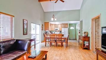 A spacious living room with a wooden ceiling, a dining area, and a kitchen in the background.