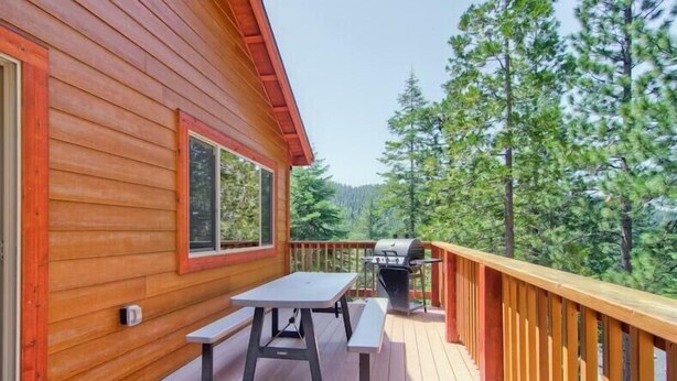 Eine Holzterrasse mit Picknicktisch und Grill, umgeben von Bäumen.