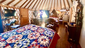 A cozy yurt interior with a bed, a television, a desk, and a chair.