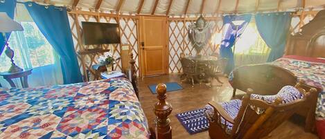 Interior acogedor de una yurta con dos camas, una silla de madera, una mesa y un televisor.