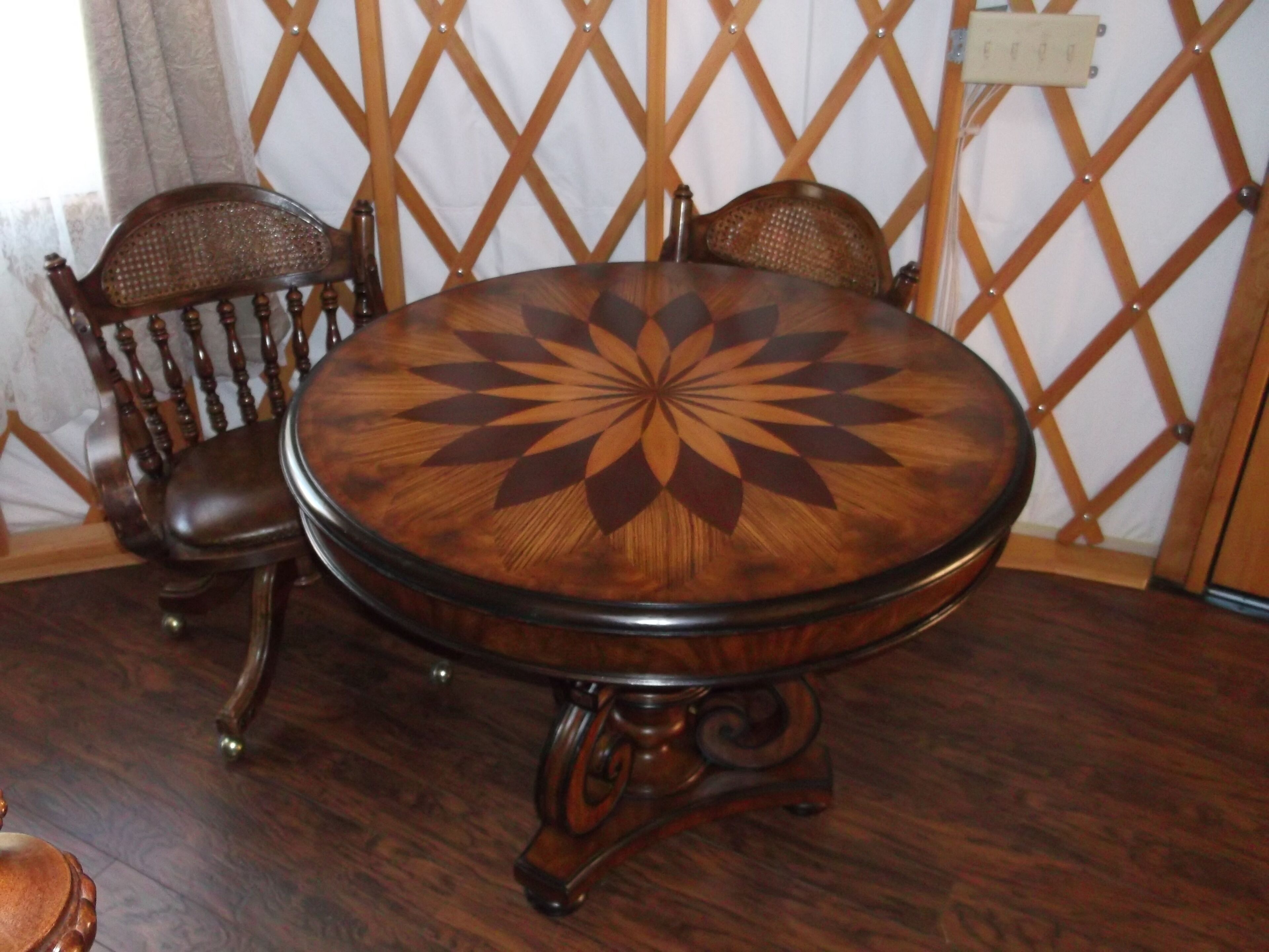 A round wooden table with a geometric pattern on the tabletop, surrounded by two upholstered chairs with wooden frames and curved backs.