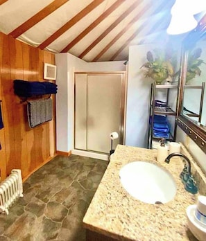 A bathroom with a stone floor, a sink with a faucet, a towel rack, and a shower door. - Yurtel Veneta - Camelot (Veneta)