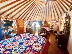 A yurt with a large bed, wooden furniture, and a television.