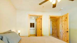 Ein Schlafzimmer mit einem Bett, einem Nachttisch und einer Lampe. Holztüren führen in andere Räume.
