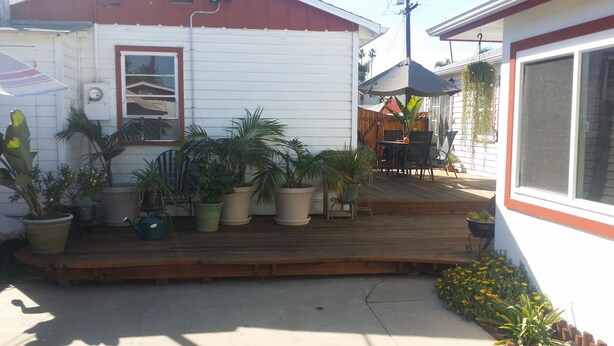 A wooden deck with potted plants, a small table with chairs, and a hanging plant.