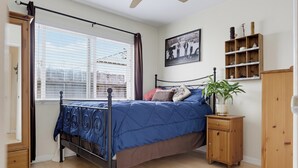 Une chambre à coucher avec un lit à baldaquin, une fenêtre avec des stores, une table de chevet agrémentée d’une plante et une étagère murale décorative.