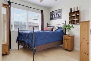 Een slaapkamer met een hemelbed, een raam met luxaflex, een nachtkastje met een plant en een wandplank met decoratieve objecten.