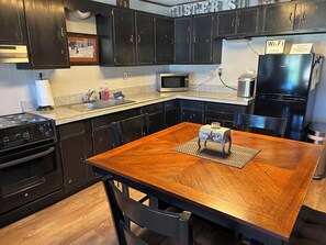 Una cocina con armarios oscuros, una mesa de comedor de madera, un microondas y un refrigerador.