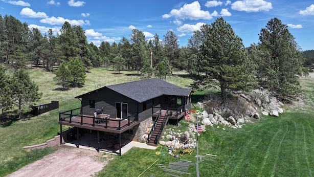 A cabin with a deck, surrounded by a grassy field and trees.
