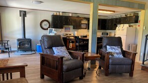 A cozy living room with two leather armchairs, a wooden coffee table, a fireplace, and a kitchen area with cabinets and appliances.