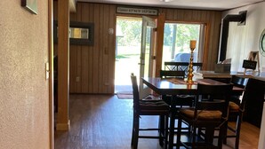 A wooden interior with a dining area featuring a table and chairs, a trash bin, and a door with a sign indicating a door code.
