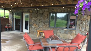 A covered patio with a stone wall, a wooden ceiling, and a table with chairs.