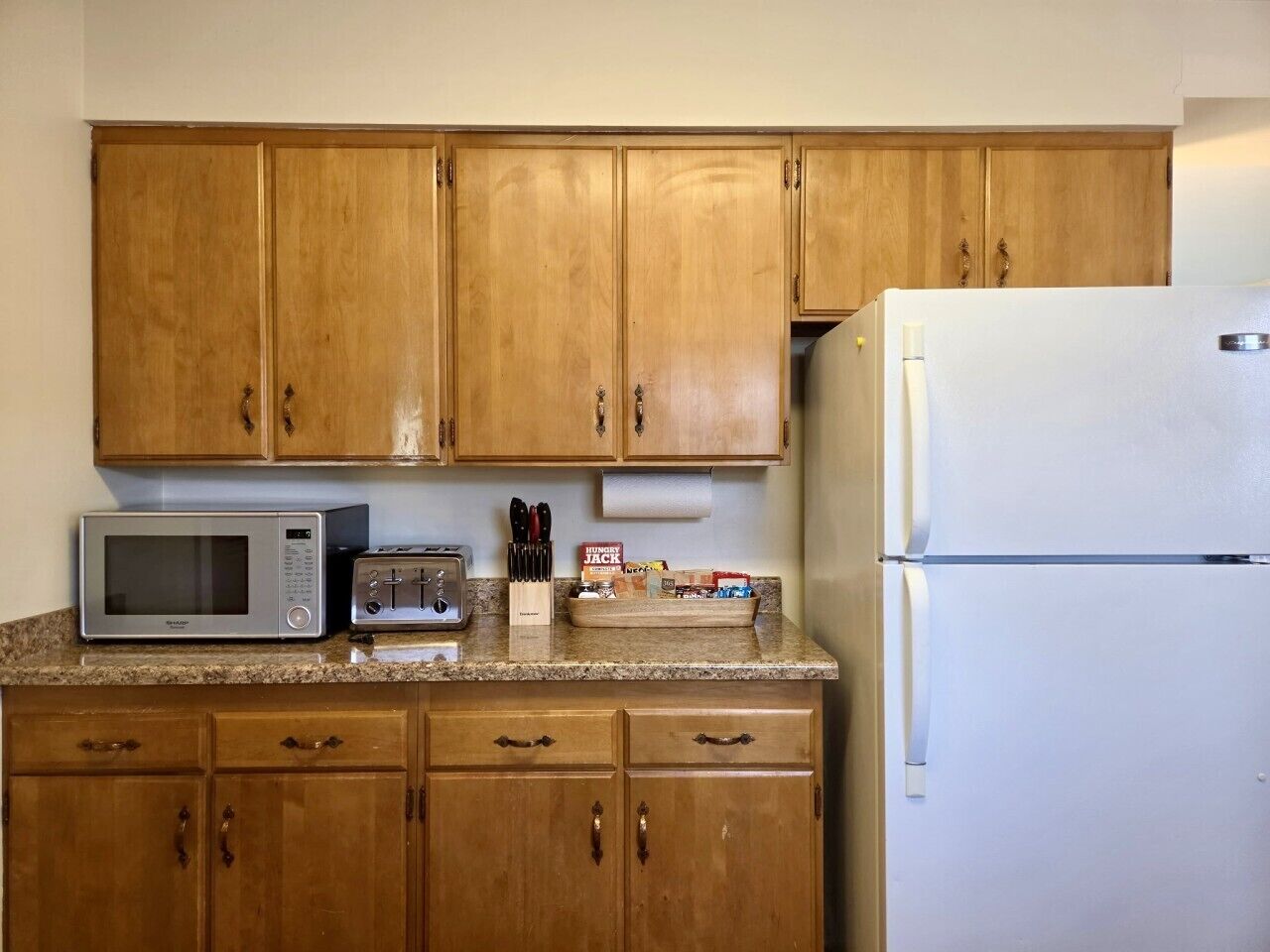 Una cocina con armarios de madera, microondas, tostadora y refrigerador.