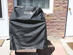 A Char-Broil grill with a black cover, placed on a brick step outside a house with a white door and a window.