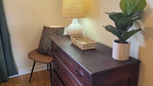 A wooden dresser with drawers, a lamp, a potted plant, and a framed picture on the wall.